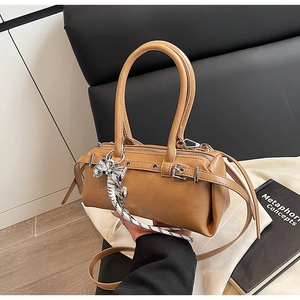 Close-up of brown Boston handbag with metal bow charm and decorative ribbon details
