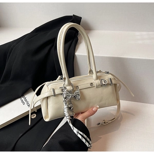 Close-up of cream Boston bag featuring long handles, metallic bow, and braided rope charm