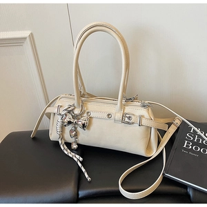 Detail of beige faux leather Boston bag with metal bow charm and adjustable strap