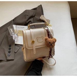 Detail van beige lederen tas met gouden kralenbeer en zachte pluche beer hanger