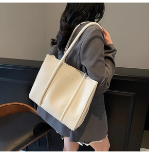 Model wearing a large off-white PU leather tote bag with FASHION embossed detail
