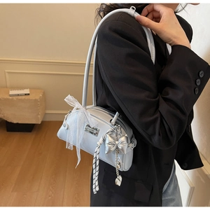 Détail du sac à bandoulière bleu clair avec pendentif nœud argenté et foulard en dentelle
