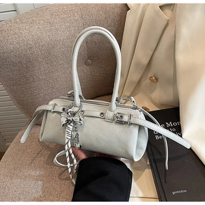 Detail of grey Boston bag with silver bow charm and leather straps on a textured chair