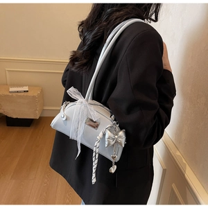 Détail du sac à bandoulière gris clair avec nœud en dentelle et pendentif cœur argenté