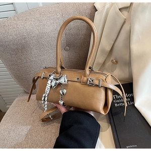 Close-up of caramel Boston bag featuring metallic charms and black-white ribbon detail