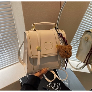Detail van beige kunstlederen mini-rugzak met gouden studs beermotief en pluche sleutelhanger