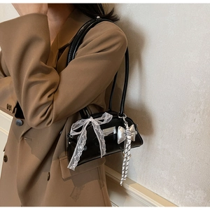 Détail du sac à bandoulière en cuir verni noir avec nœud en dentelle blanche et bijou