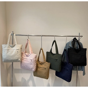 Rack of colorful quilted nylon tote bags featuring a front zipper pocket and long handles