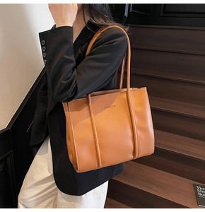 Detail of a brown leather tote bag with double handles shown in a lifestyle indoor setting