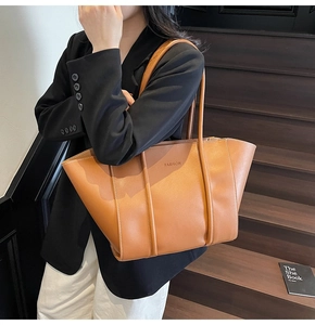 Detail of a brown leather tote bag with FASHION engraving shown on a shoulder