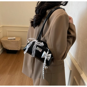 Détail d'un sac à bandoulière noir brillant avec nœud en dentelle et pendentif papillon