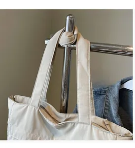 Close-up of beige tote bag with wide handle and zip top hanging on a metal rack