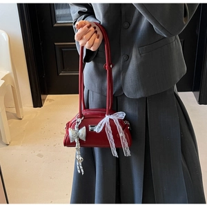Détail du sac à bandoulière rouge avec nœud en dentelle et pendentif logo métallique