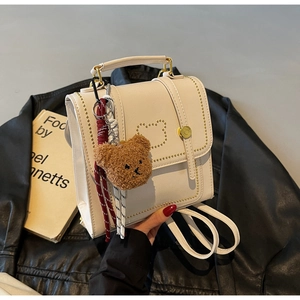 Detail van de crème mini-rugzak met gouden berenlogo en zachte pluche hanger