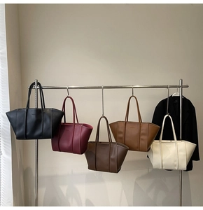 Detail view of large matte leather tote bags in five assorted colors hanging on a rack