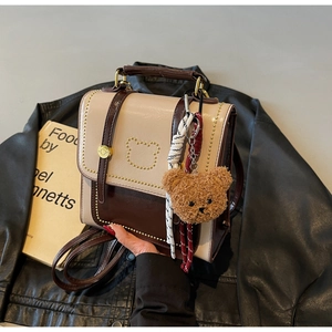 Detail van mini-rugzak met berenpatroon van klinknagels en pluche hanger op leren jas
