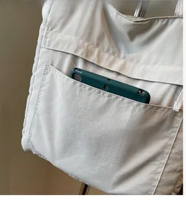 Detail of a large beige tote bag featuring a functional front pocket holding a green phone