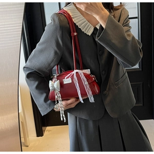 Détail du sac à main en cuir verni rouge foncé avec nœud en dentelle et breloques
