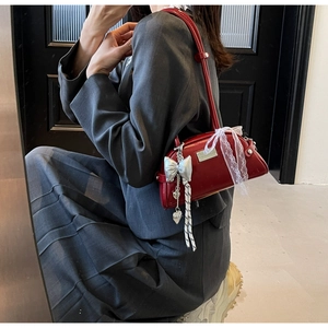 Détail d'un sac à bandoulière rouge brillant avec charms argentés et nœud en dentelle