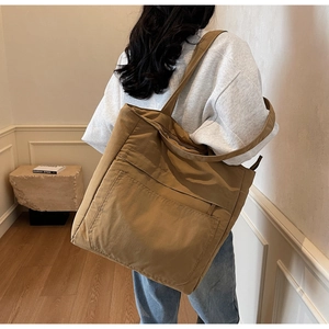 Brown high-capacity tote bag with front pocket shown on shoulder in a cozy home setting