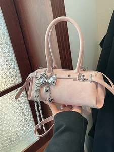 Light pink PU Boston handbag with silver bow charm and adjustable strap held by a model