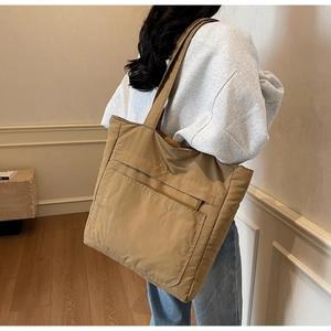 Large khaki canvas tote bag with front pocket shown on shoulder for daily school use
