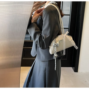 Sac hobo crème chic avec rubans en dentelle et pendentif porté par un mannequin