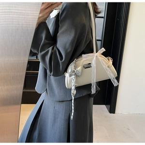 Détail du sac demi-lune beige avec pendentif nœud argenté et dentelle élégante