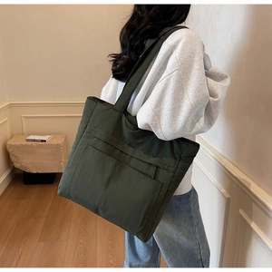Detail of dark green large capacity nylon tote bag worn over the shoulder by a model