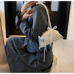 Détail du sac crème avec breloque nœud argenté et ruban dentelle sur blazer gris