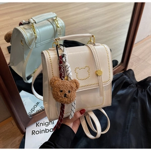 Detail van een roomwitte mini-rugzak van glanzend PU-leer met gouden berenkop versieringen