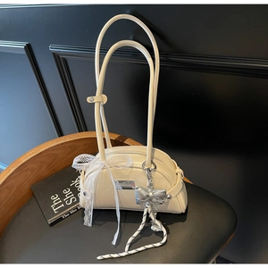 Détail du sac crème avec un grand nœud en dentelle et un pendentif papillon argenté