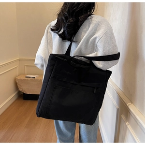 Rear view of model wearing a black nylon tote bag with multiple straps and pockets