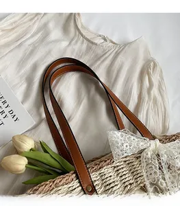 Détail des bretelles en cuir marron durable sur un grand sac fourre-tout en paille