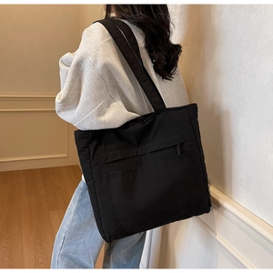 Practical black nylon tote bag with side zip pockets shown on a shoulder in a soft interior