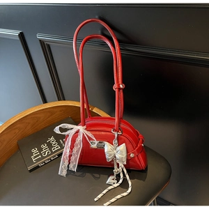 Gros plan sur un sac rouge verni avec nœud en dentelle blanche et pendentif cœur argenté