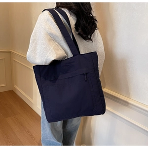 Detail view of a large navy blue nylon tote bag with front zipper pocket on a model