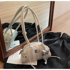 Détail du sac à bandoulière beige avec nœud en dentelle blanche et pendentifs argentés