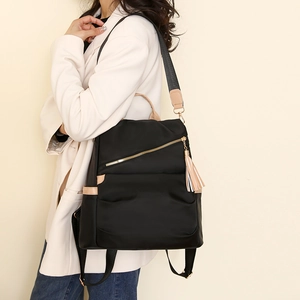 Detail of black nylon anti-theft backpack with beige trim and stylish tassel on model