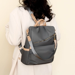 Detail of grey nylon anti-theft backpack with brown leather trim and tassel accent