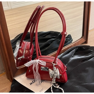 Détail du sac rouge en cuir avec pendentif nœud argenté et ruban en dentelle blanche