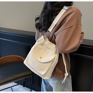 Dettaglio di una borsa a secchiello in tela beige con tracolla larga e tasca frontale