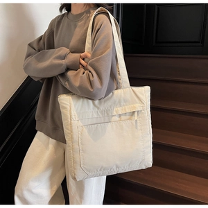 Close-up of cream quilted tote bag with front pocket showing soft padded fabric texture