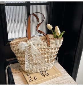 Détail du sac cabas en paille tissé avec nœud en dentelle blanche et anses en cuir