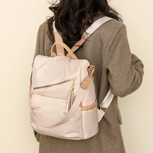 Detail of a beige nylon backpack with elegant tassel charm and metal zipper on model