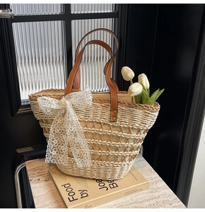 Détail du sac cabas en paille avec des anses marron et un grand nœud en dentelle blanche