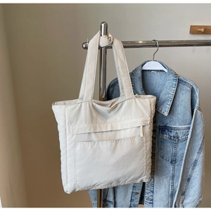 Detail of a large beige nylon tote bag hanging with a denim jacket on a metal hanger