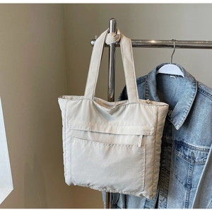 Detail view of large front pocket on beige canvas tote bag with wide shoulder strap