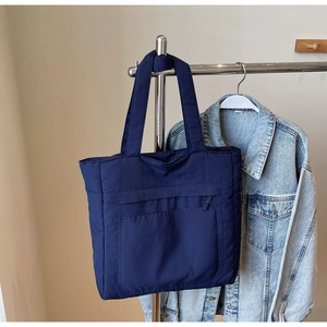 Detail of navy blue tote bag with front pocket and zip accent hanging on hanger