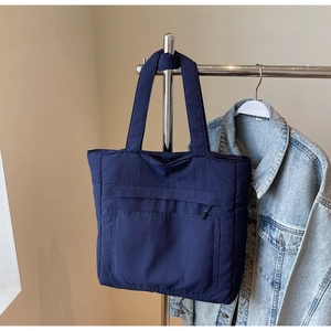 Detail of navy blue tote bag featuring matte nylon fabric and functional front zip pocket